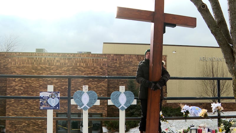 Dan Beazley stands with the homemade cross he brought from Michigan for victims of a shooting...
